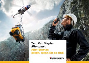 Hubschrauber fliegt mit Gabelstapler als hängende Last über Felsenwand