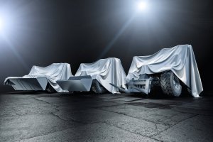 Drei mit Tüchern verhüllte Liebherr Teleskoplader im Scheinwerferlicht vor dunklem Hintergrund auf Asphalt
